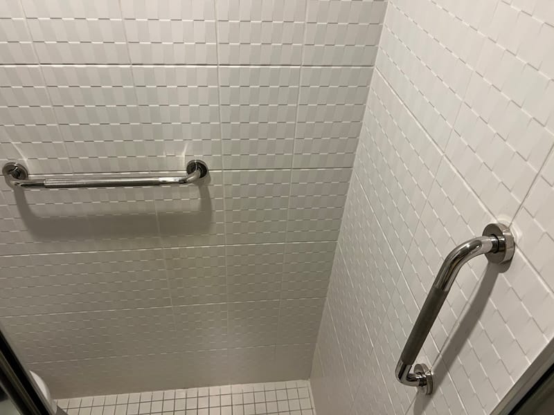 Chrome grab bars installed in a tiled shower for accessibility